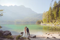 Bride and groom sharing a joyful laugh by the lakeside at sunset.