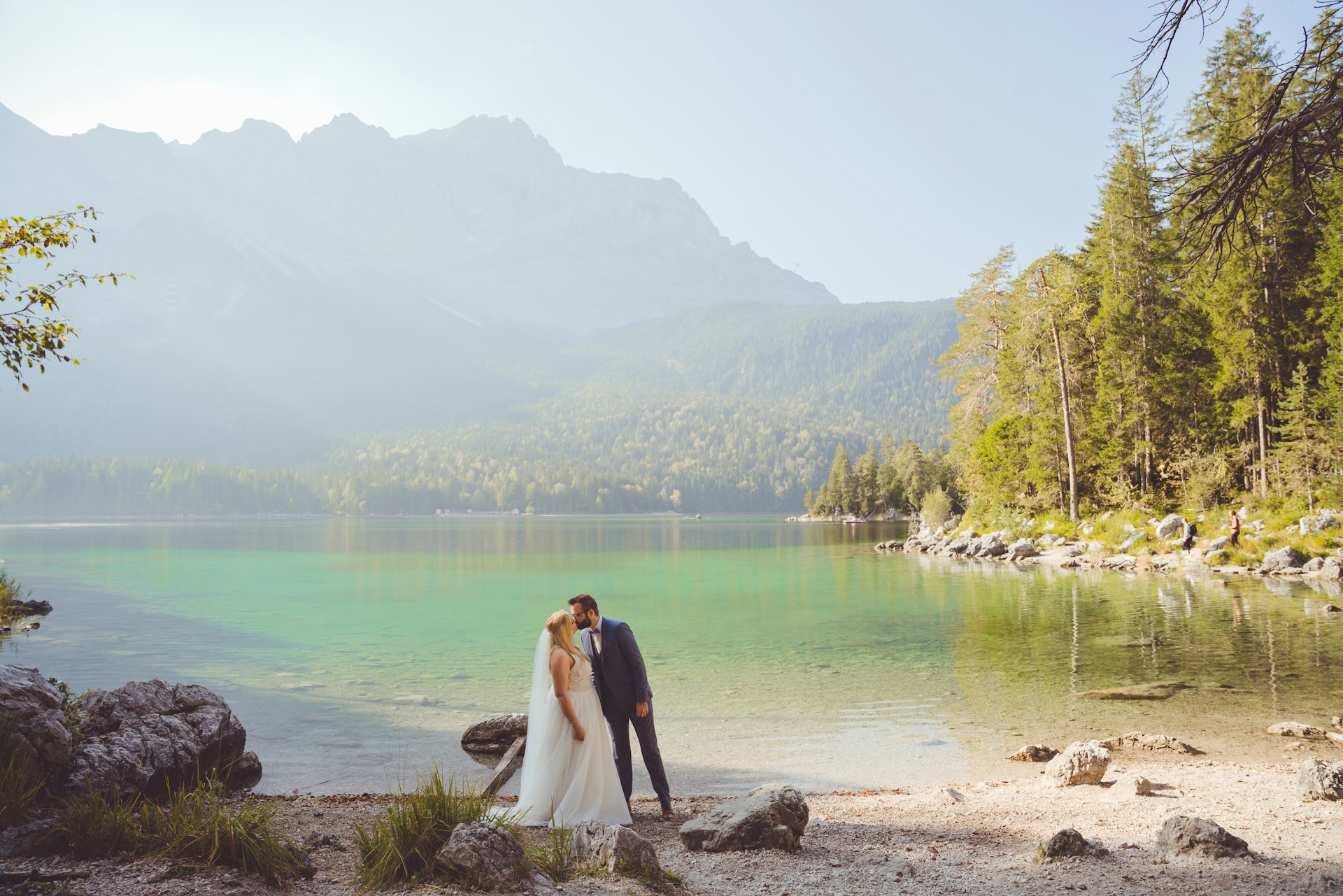 A couple on a honeymoon tour walking hand in hand along the tranquil shores of a crystal-clear lake framed by snow-capped peaks.