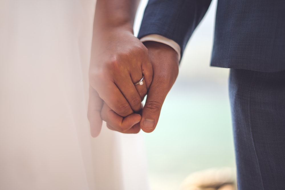 hombre en chaqueta de traje negro tomado de la mano con mujer en vestido blanco