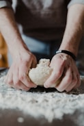 person holding white dough on brown wooden table