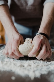 Close-up of a baker’s hands kneading sourdough dough on a floured wooden table.
