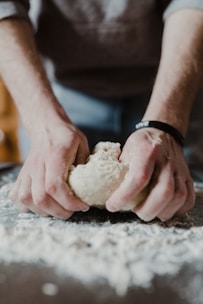 A close-up of a person’s hands kneading dough on a wooden kitchen counter.