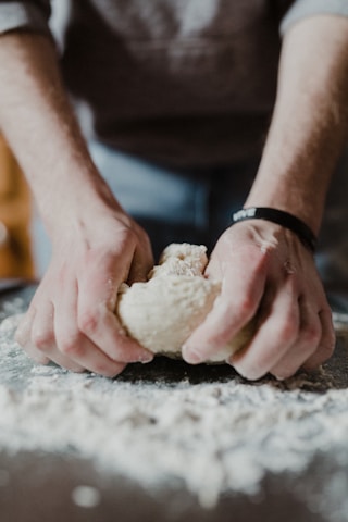 Close-up of a baker's hands kneading dough on a floured surface.
