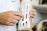 A person in a white lab coat is holding a white, 3D-printed object that resembles a custom orthopedic brace. The object has a lattice structure with several openings. The background suggests a workshop or laboratory environment.