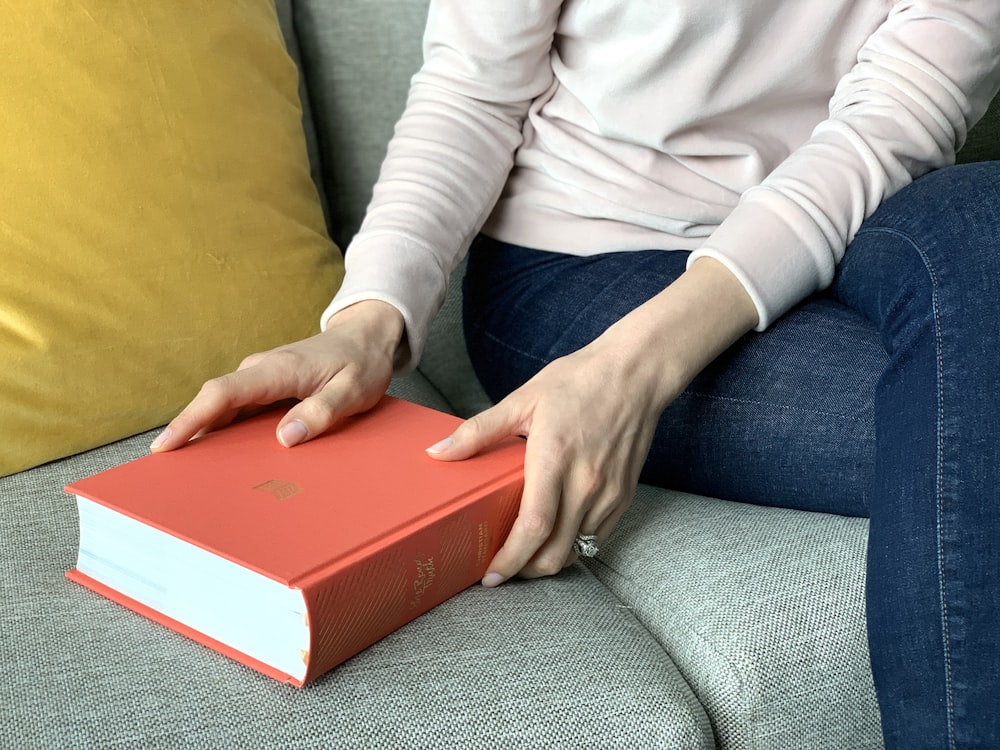 person in white long sleeve shirt and blue denim jeans sitting on gray sofa