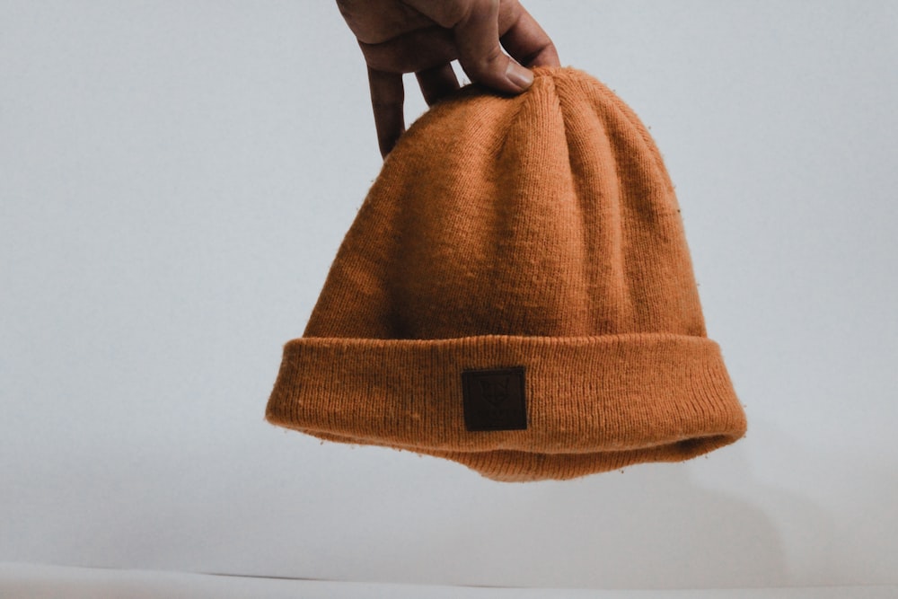 a hand holding a brown hat on top of a white surface