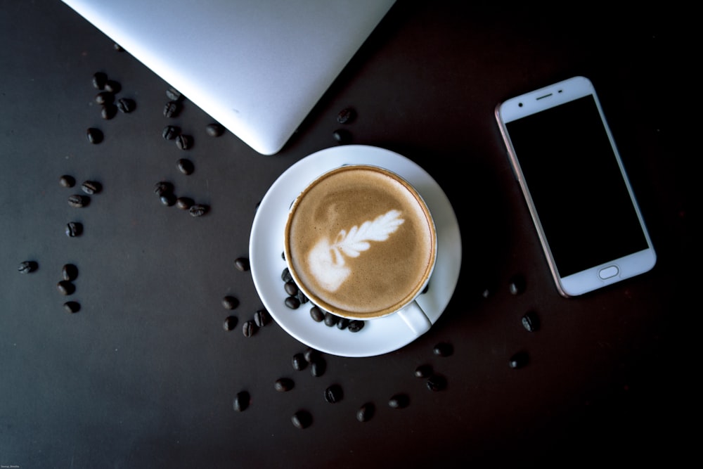 white ceramic cup on saucer beside silver iphone 6