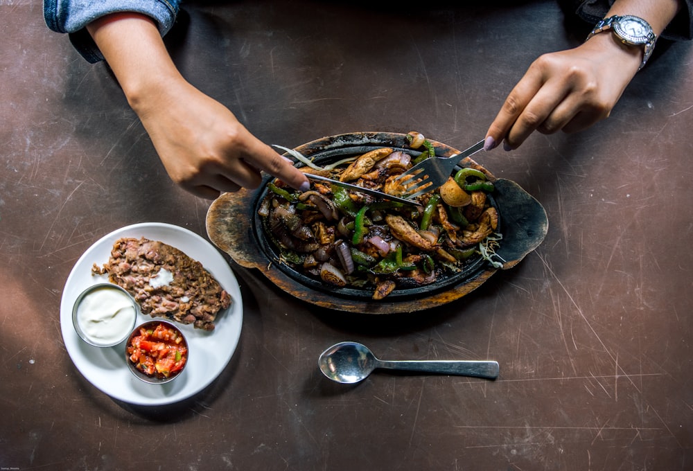 person holding stainless steel spoon and bowl with food