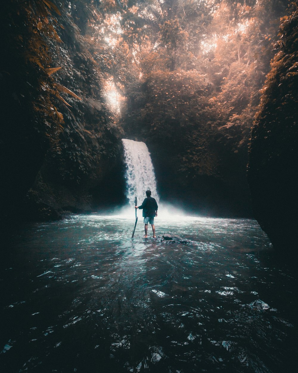 person in black jacket standing on water between rock formation during daytime