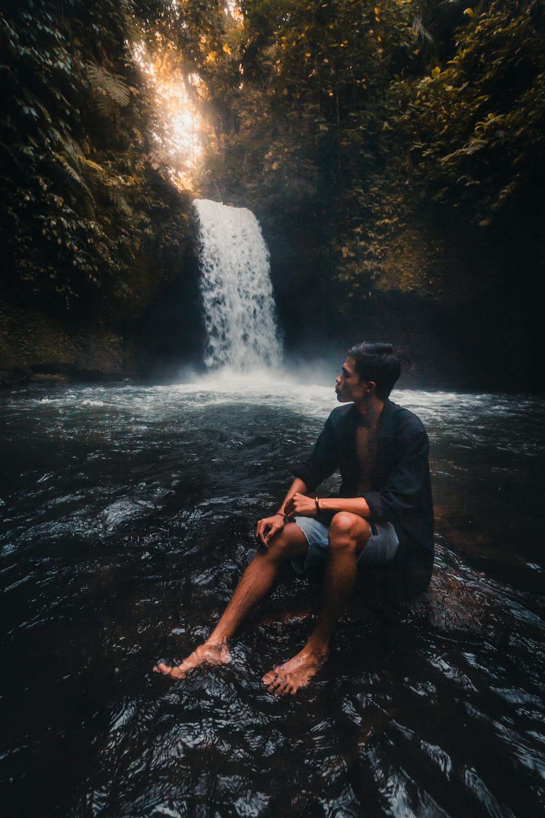woman in black shirt sitting on rock near waterfalls during daytime