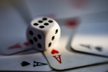 A blurred close-up image of a white dice with black dots surrounded by playing cards displaying the ace of hearts and ace of spades.