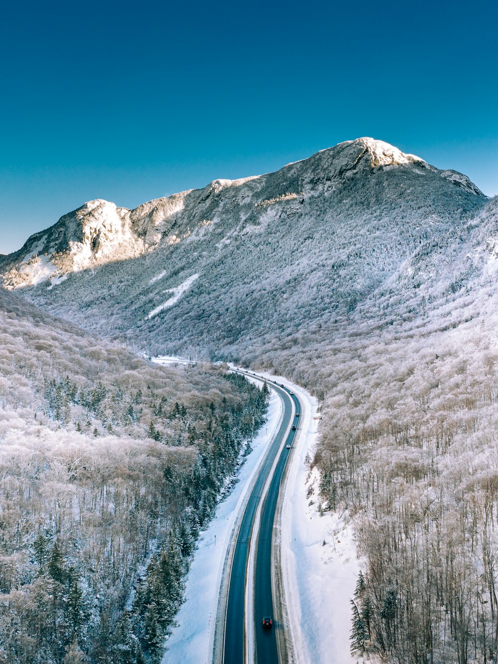 snow covered road near mountain under blue sky during daytime
