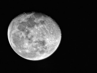 A detailed view of the moon's surface with visible craters and rough textures. The moon appears bright against a dark background, emphasizing its round and uneven terrain.