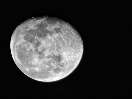 A detailed view of the moon's surface with visible craters and rough textures. The moon appears bright against a dark background, emphasizing its round and uneven terrain.