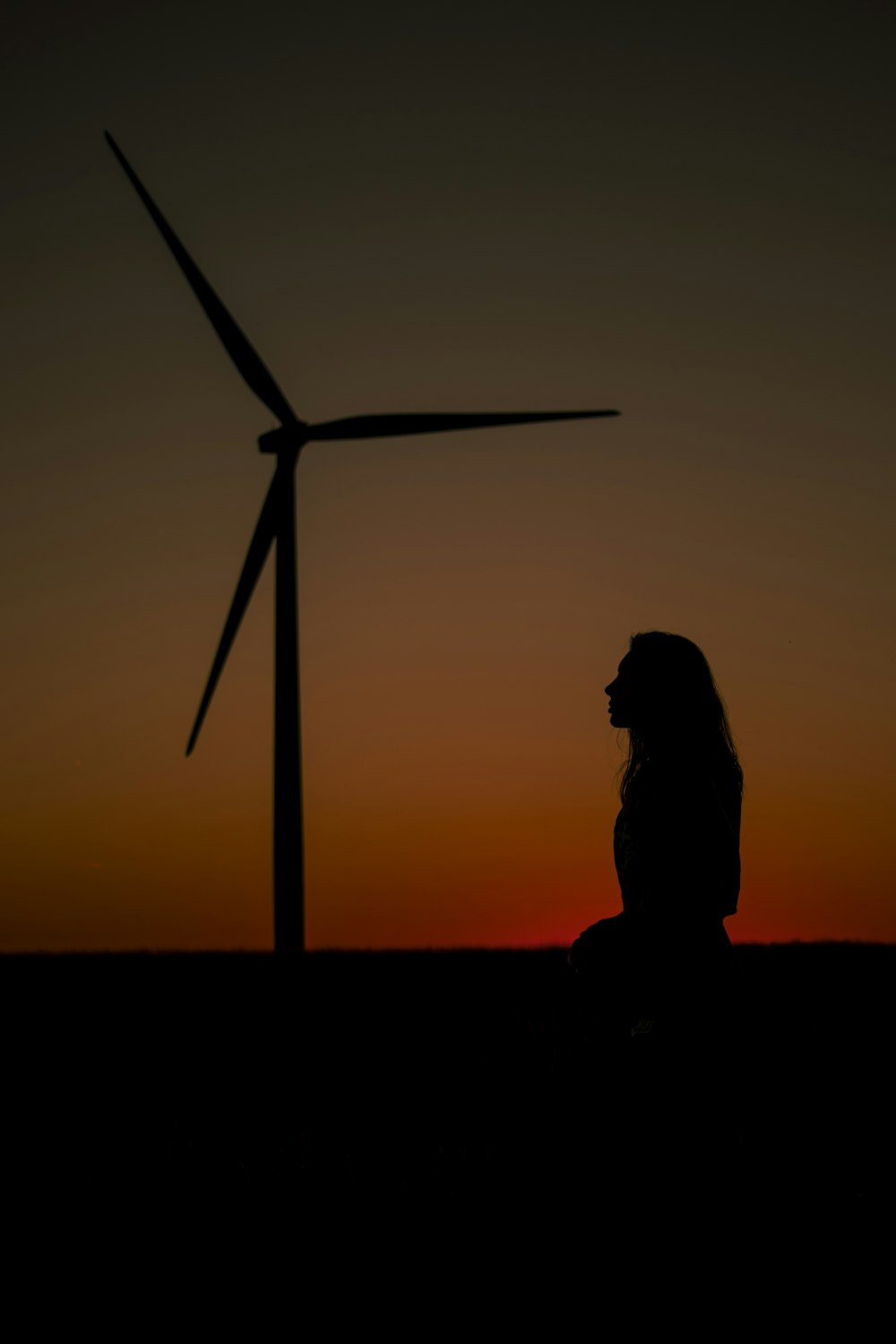 Silueta de la persona de pie cerca del molino de viento durante la puesta del sol