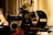 A vintage film camera, specifically an Arriflex 16SR, is positioned on a tripod. The camera features detailed dials, knobs, and labels. The setting includes a blurred curtain backdrop, creating a nostalgic and professional atmosphere.