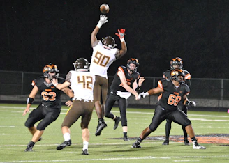 A dynamic shot of a flag football game in action, with players reaching for the ball under bright stadium lights.