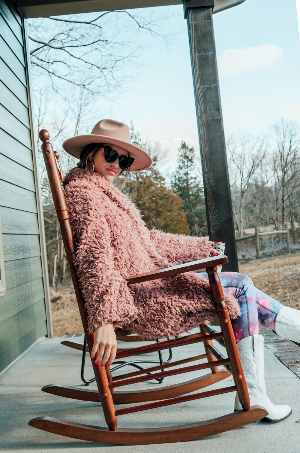 woman in brown coat and brown hat sitting on brown wooden chair