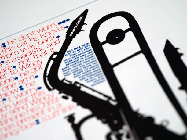 A close-up image features a silhouette of a musical instrument, likely a saxophone, juxtaposed against stylized text in varying fonts and colors. The text comprises phrases in red and blue, with some parts underlined in blue dots, contributing an artistic and graphic design element.