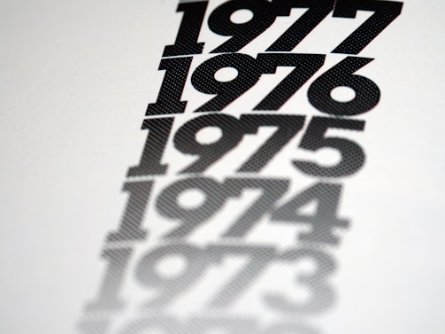 A series of bold, black numbers arranged vertically on a white background, each following the previous year chronologically: 1977, 1976, 1975, 1974, and 1973. The numbers appear to fade into the background, creating a shadow effect.
