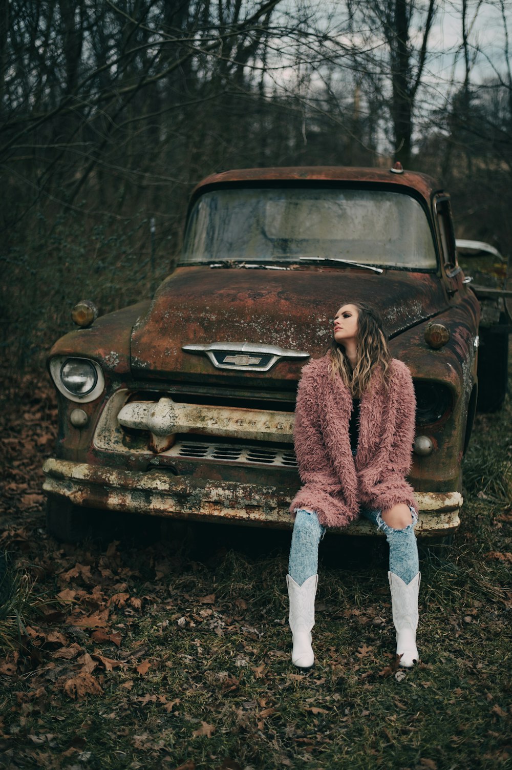 woman in brown sweater and blue denim jeans standing beside brown car