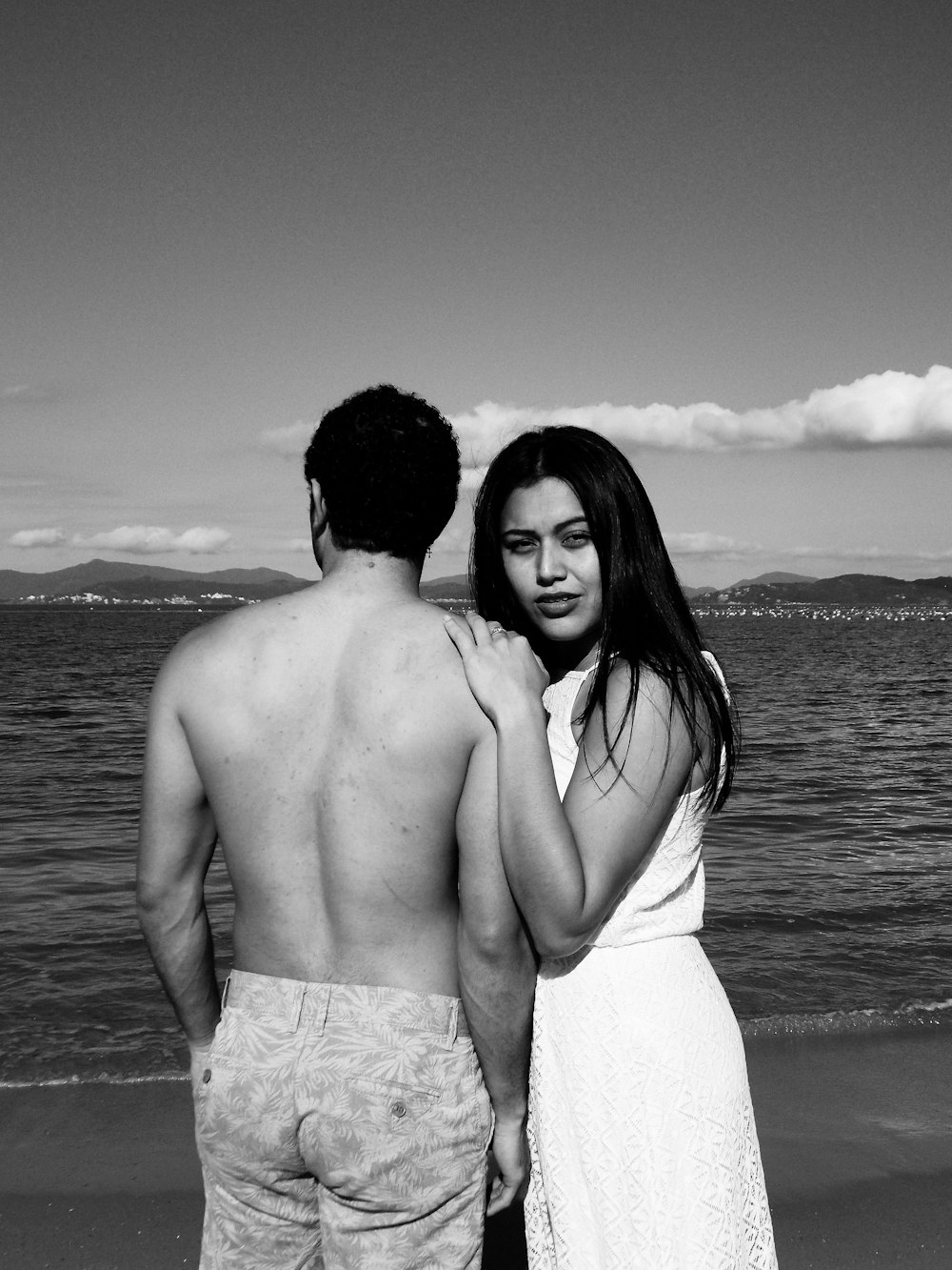 Foto en escala de grises de una pareja de pie en la playa