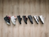 A collection of seven different sneakers lined up on a wooden floor, showcasing a variety of designs and colors.