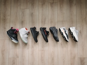 A collection of seven different sneakers lined up on a wooden floor, showcasing a variety of designs and colors.