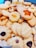 A variety of homemade cookies are arranged together. They include different shapes such as stars and flowers, with textures that appear soft and crumbly. Some cookies are topped with raisins or pieces of fruit, adding visual appeal.