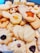 A variety of homemade cookies are arranged together. They include different shapes such as stars and flowers, with textures that appear soft and crumbly. Some cookies are topped with raisins or pieces of fruit, adding visual appeal.