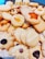 A variety of homemade cookies are arranged together. They include different shapes such as stars and flowers, with textures that appear soft and crumbly. Some cookies are topped with raisins or pieces of fruit, adding visual appeal.