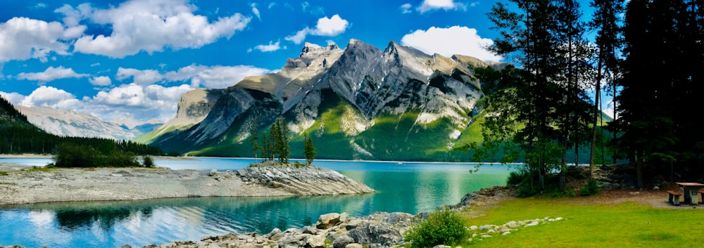 lake near green trees and mountain under blue sky during daytime