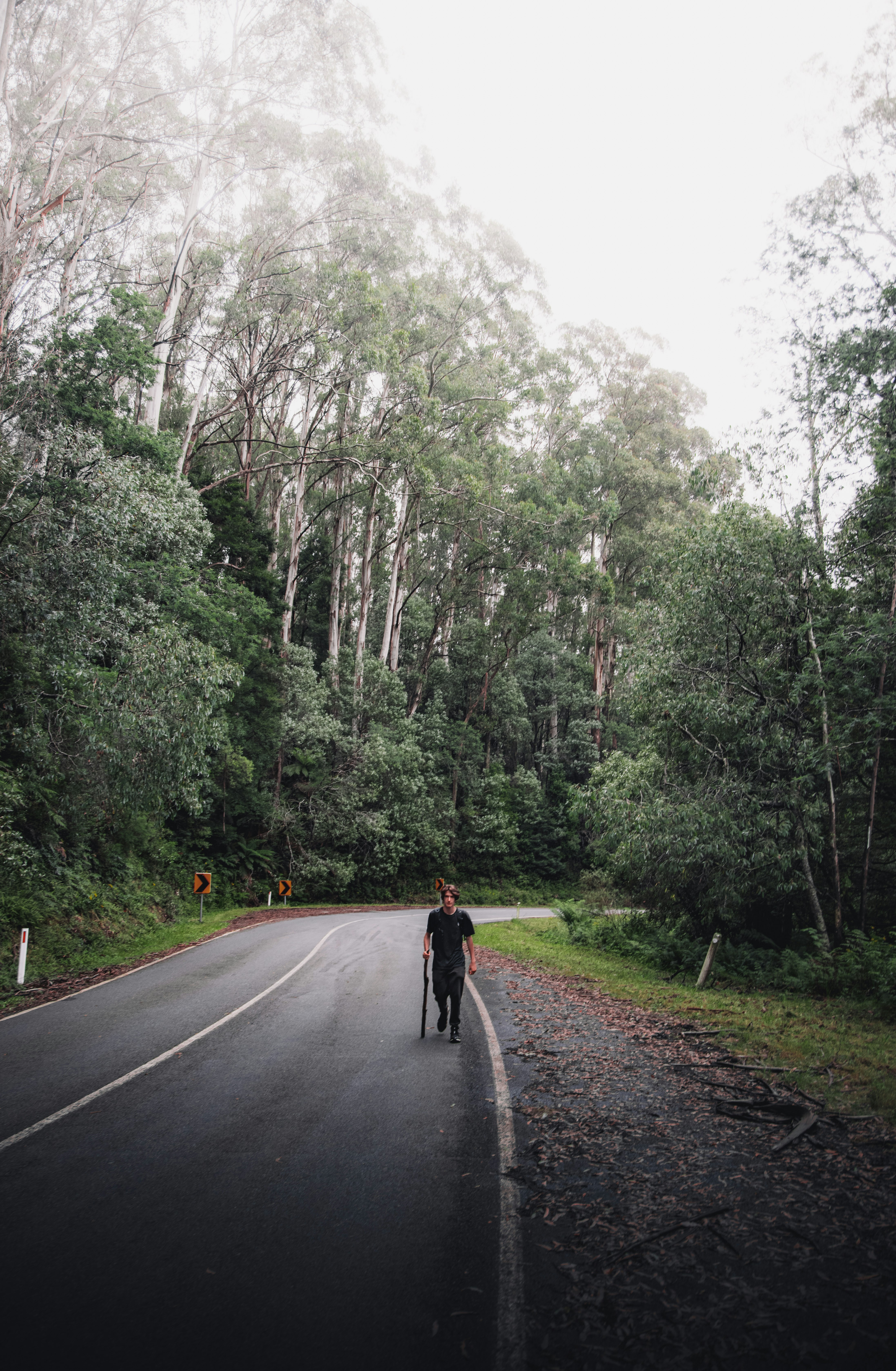 person in black jacket walking on gray asphalt road during daytime