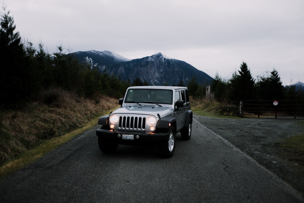 white jeep wrangler on road near green grass field and mountain during daytime