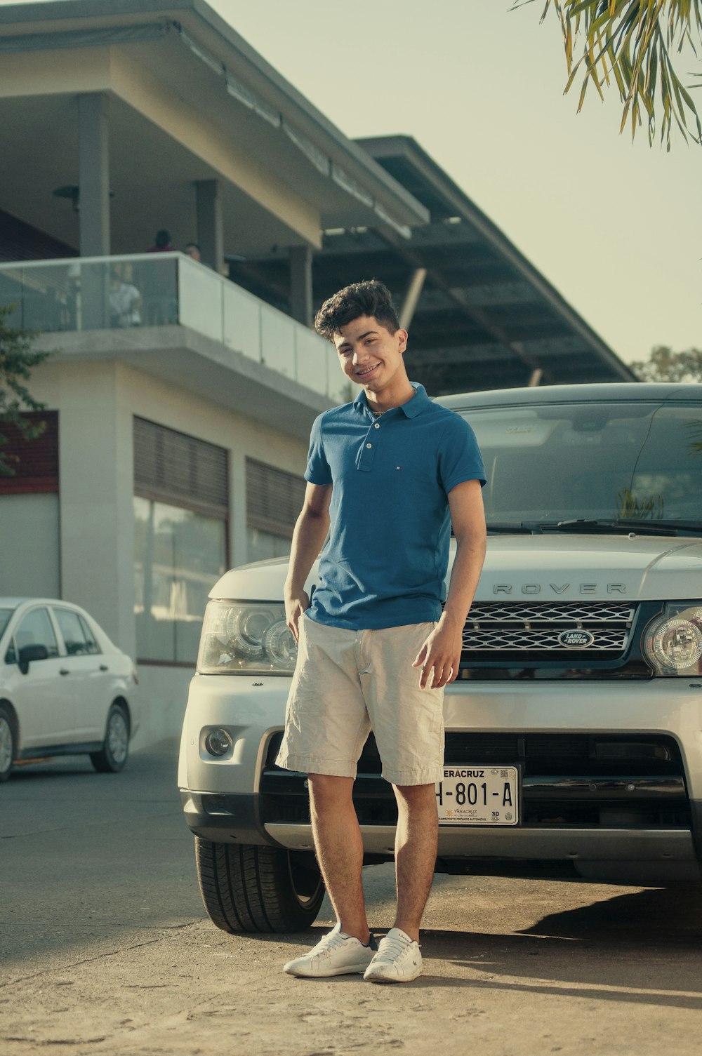 man in blue polo shirt and brown shorts standing beside silver mercedes benz car