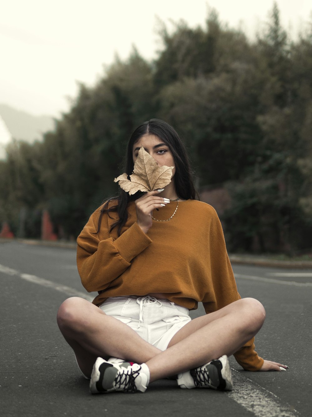 woman in brown coat sitting on road during daytime