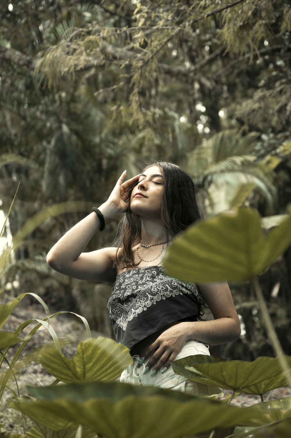 woman in black and white floral sleeveless dress sitting on green leaf plant during daytime