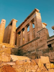 A sunlit view of ancient Greek temple ruins with towering stone columns against a clear blue sky.