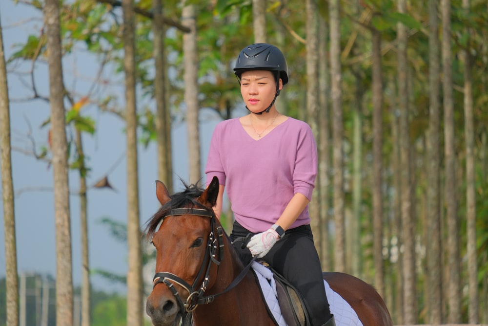 Femme en t-shirt à col rond rose équitation sur un cheval brun pendant la journée