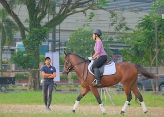 woman in blue jacket and blue denim jeans riding brown horse during daytime