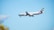 A large commercial airplane with the Emirates logo is flying against a clear blue sky. The aircraft features distinct markings on the tail and appears to be preparing for landing as the landing gear is extended.