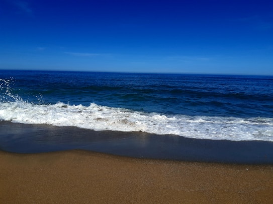 A tranquil beach scene with gentle waves lapping onto the sandy shore under a deep blue sky.