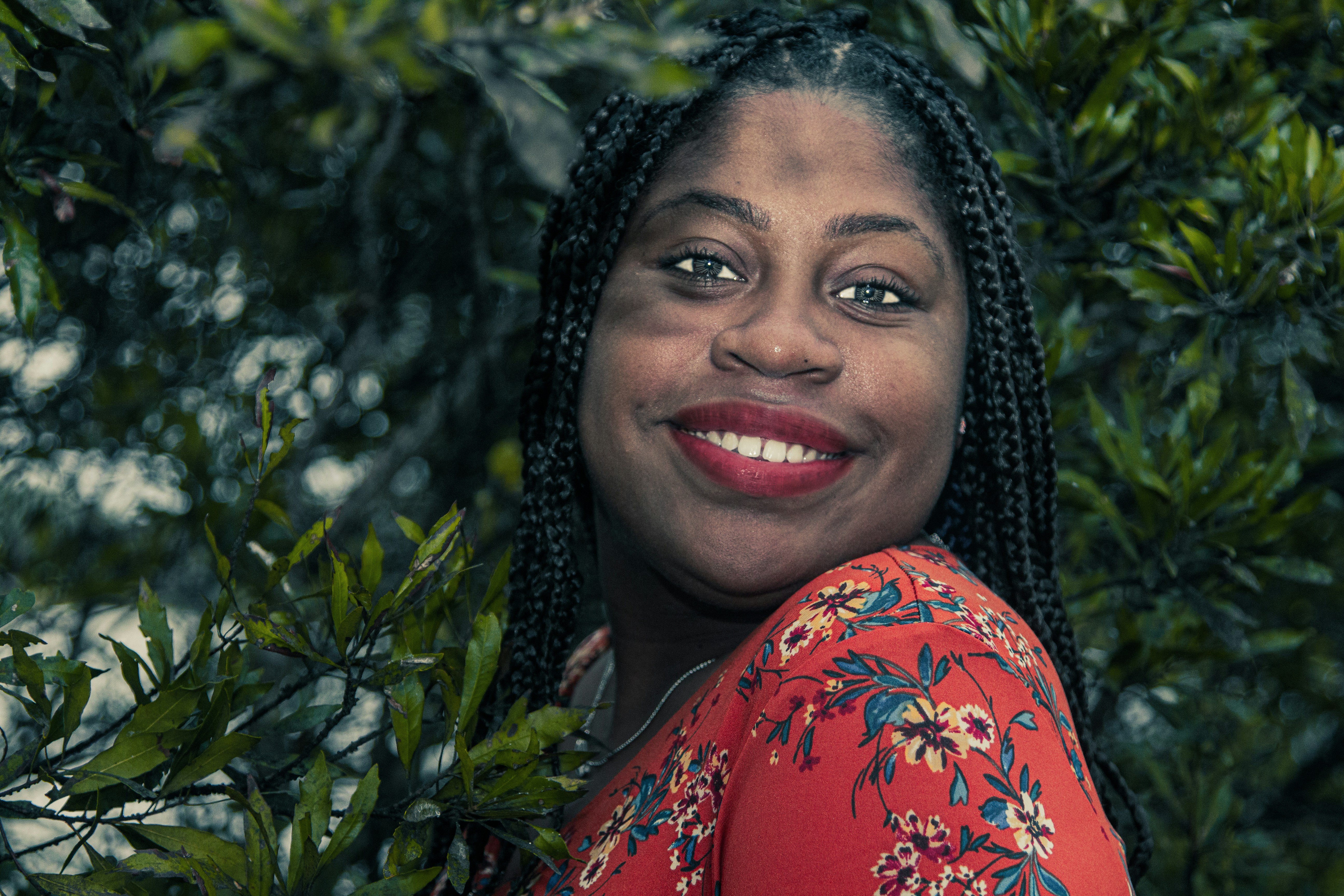 Professional headshot of African woman with long braided hair wearing red top smiling warmly