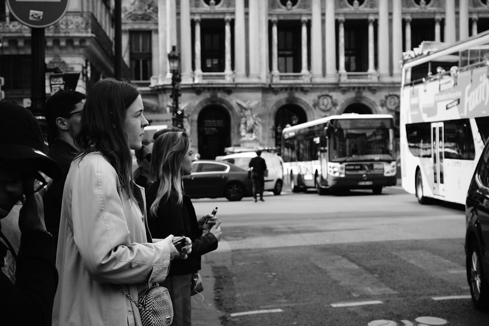 grayscale photo of woman in white coat and black and white checked pants holding black dslr