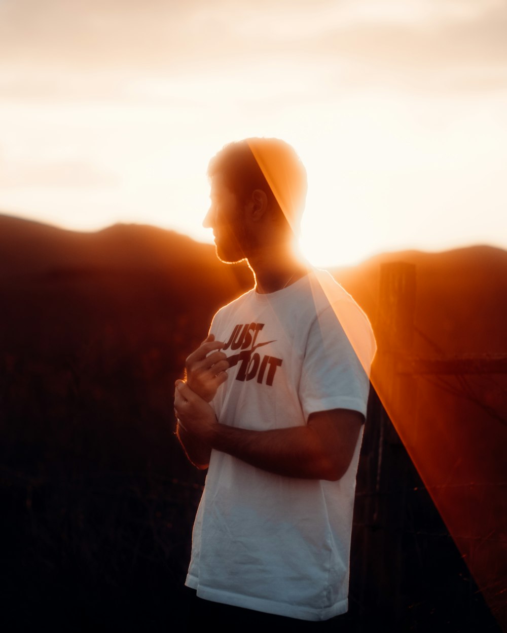 man in white crew neck t-shirt standing on top of mountain during sunset