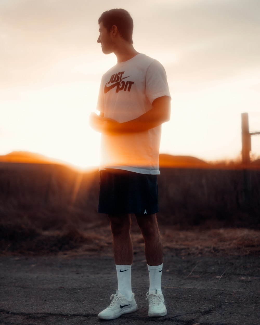 man in white crew neck t-shirt and black shorts standing on brown field during sunset