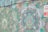The image features a vibrant mural with intricate mandala patterns and swirling floral designs. Colors range from various shades of green to hints of purple, orange, and white. There is a bold, partially visible sign in the top right corner with contrasting red and white colors.