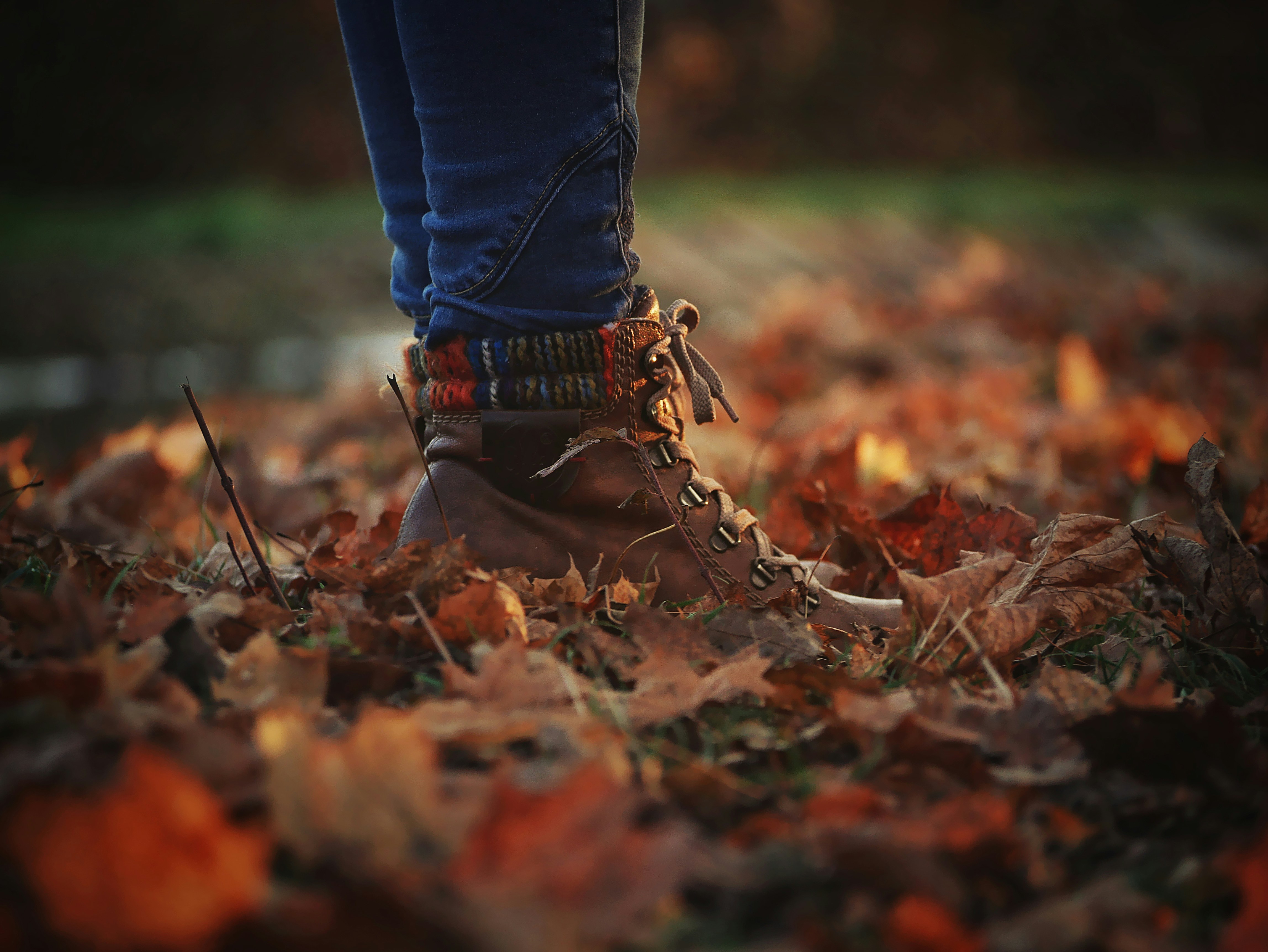 person in blue denim jeans and brown boots standing on dried leaves