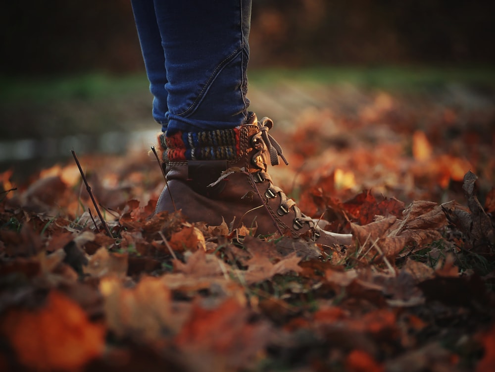 personne en jean bleu et bottes marron debout sur des feuilles séchées