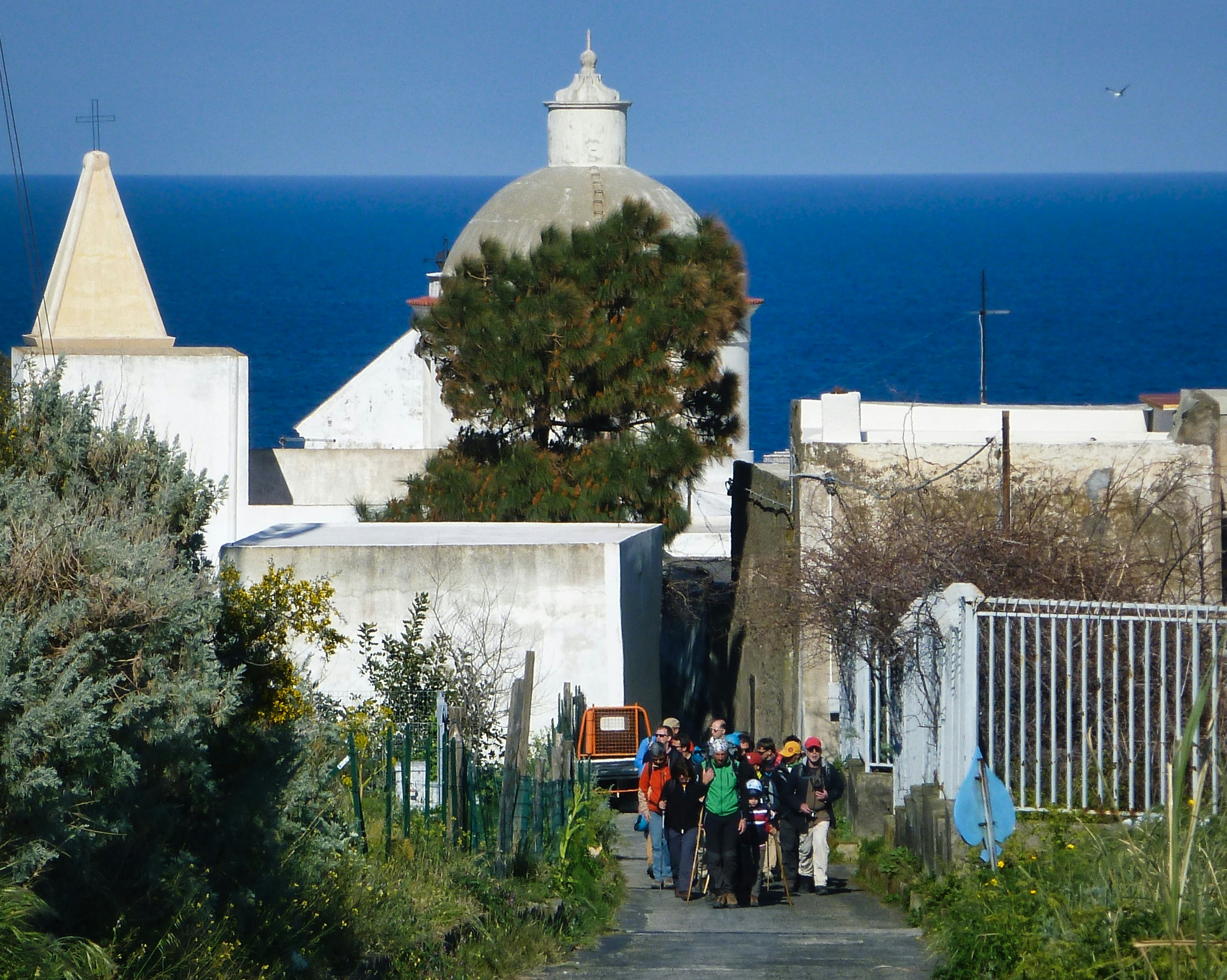 Turisti passeggiano lungo un sentiero lastricato in una cittadina costiera.